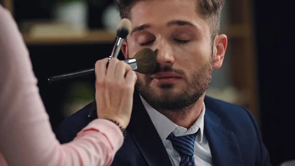 Blurred woman doing makeup to young man with closed eyes — Stock Photo