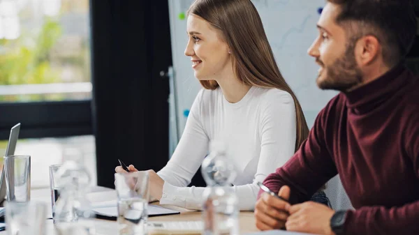 Junge Geschäftsfrau lächelt neben verschwommenem Kollegen im Besprechungsraum — Stockfoto