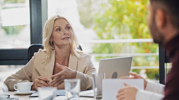 Geschäftsfrau mittleren Alters zeigt mit der Hand auf verschwommene Manager im Büro — Stockfoto