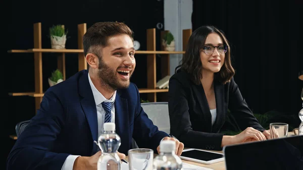 Jovem empresário rindo perto de colega sorridente na sala de reuniões — Fotografia de Stock