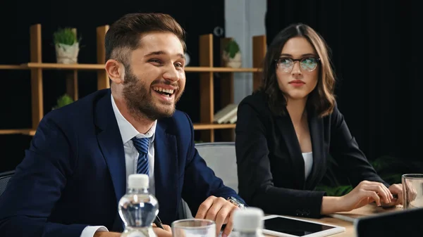 Jungunternehmer lacht bei Treffen neben ernsthafter Frau mit Brille — Stockfoto