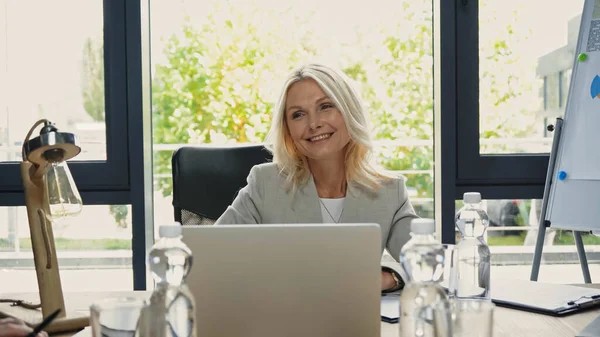Femme d'affaires d'âge moyen souriant près d'un ordinateur portable dans la salle de réunion — Photo de stock