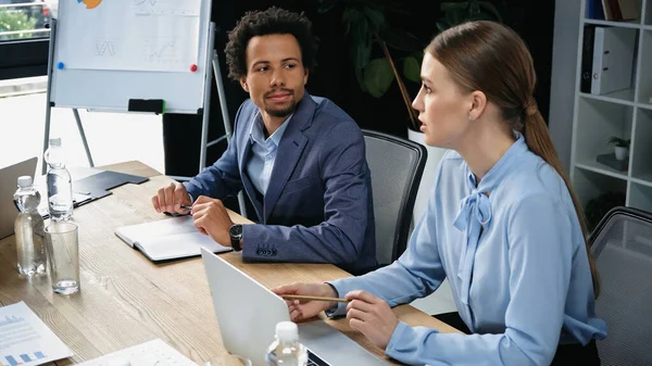 Interracial business partners sitting near laptop and documents in meeting room — Stock Photo
