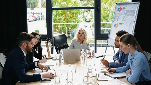 Multiethnic business partners working at desk with gadgets and documents in meeting room — Stock Photo