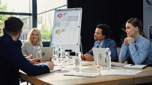 Middle aged businesswoman smiling during meeting with young multiethnic managers — Stock Photo