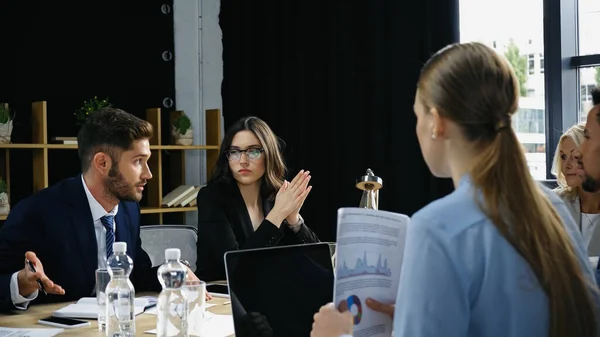 Homem apontando com a mão enquanto conversa com colegas multiétnicos durante reunião de negócios — Fotografia de Stock