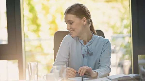 Счастливая деловая женщина улыбается в конференц-зале рядом с размытыми стаканами воды — стоковое фото