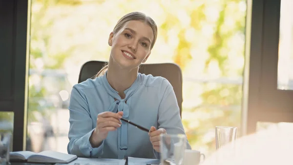 Young businesswoman holding pen while smiling at camera in office — Stock Photo