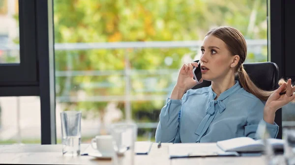 Молодая деловая женщина разговаривает по мобильному телефону в офисе на размытом переднем плане — стоковое фото
