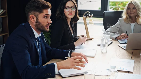 Joven gerente hablando durante la reunión de negocios con colegas - foto de stock