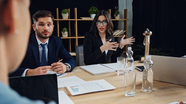 Mujer de negocios en gafas de vista señalando con las manos durante la reunión con colegas - foto de stock