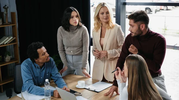 Young manager pointing with finger while talking to interracial colleagues in meeting room — Stock Photo
