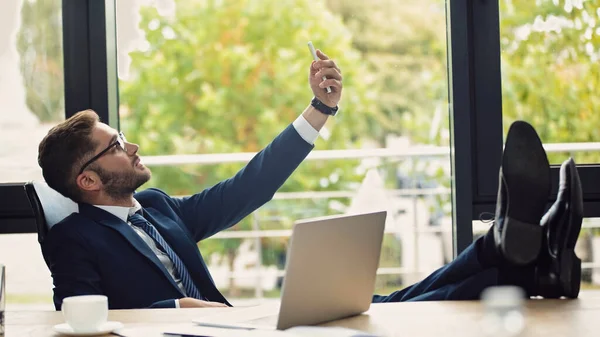 Businessman in formal wear taking selfie while sitting near laptop with legs on desk — Stock Photo