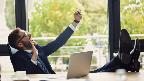 Homme d'affaires excité assis avec les jambes sur le bureau et agitant la main tout en prenant selfie sur smartphone — Photo de stock