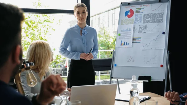 Young woman standing near flipchart during business meeting with interracial colleagues — Stock Photo