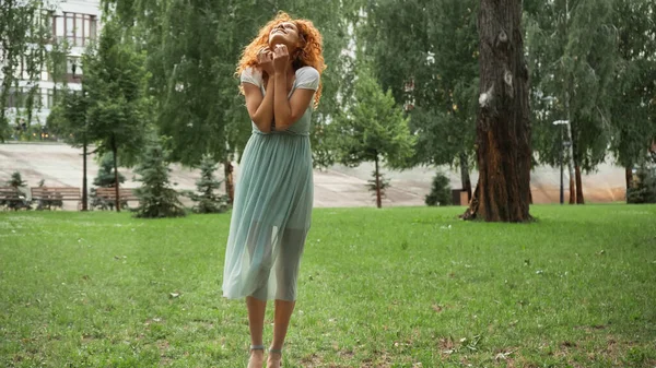 Весела руда жінка в шифонній сукні, що стоїть в зеленому парку — стокове фото