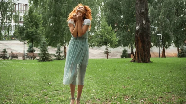 Alegre pelirroja en vestido de gasa de pie en el parque verde - foto de stock