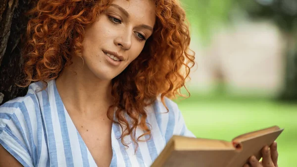 Lockige rothaarige Frau liest Buch im Park — Stockfoto