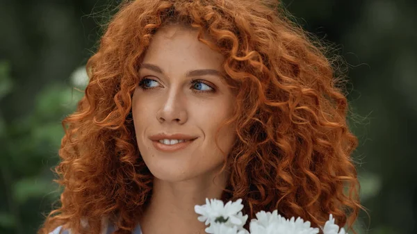 Rousse bouclée femme aux yeux bleus près des fleurs blanches — Photo de stock