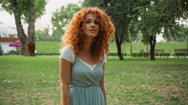 Pretty redhead woman looking at camera while standing in park — Stock Photo