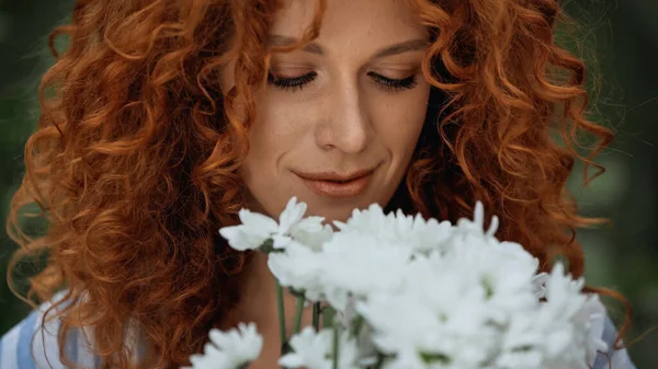 Close up de encaracolado ruiva mulher olhando para flores brancas — Fotografia de Stock