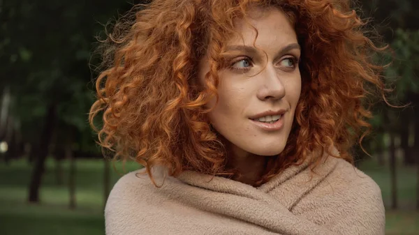 Pretty redhead woman covered in blanket smiling while looking away outside — Stock Photo