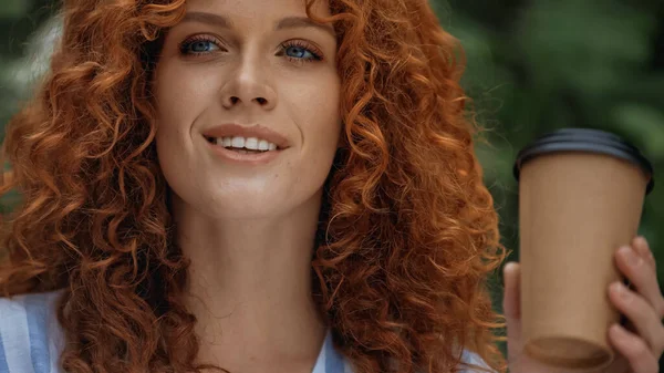 Cheerful redhead woman with blue eyes holding paper cup outside — Stock Photo
