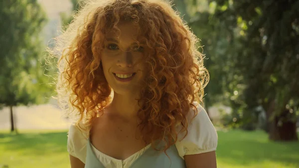 Сонячне світло на кучеряве волосся жінки, посміхаючись у парку — стокове фото
