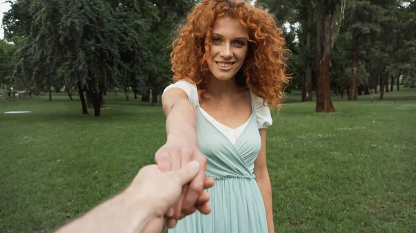 Мужчина, держащийся за руки с веселой рыжей женщиной в зеленом парке — стоковое фото