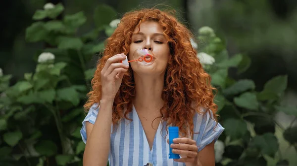 Ricci rossa donna che soffia bolla di sapone nel parco — Foto stock