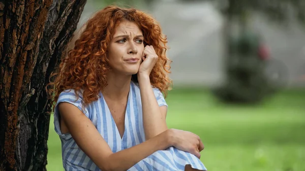 Triste jovem mulher com cabelo vermelho olhando para longe no parque — Fotografia de Stock