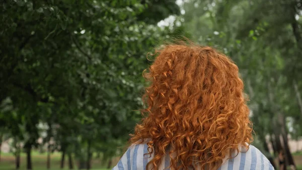 Mujer joven y rizada con el pelo rojo en el parque verde - foto de stock