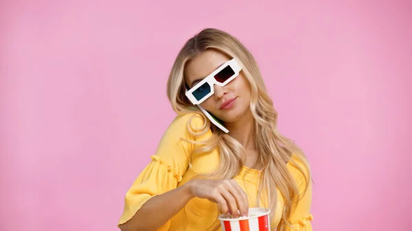 Женщина в 3D очках разговаривает на смартфоне и держит попкорн изолирован на розовый — стоковое фото