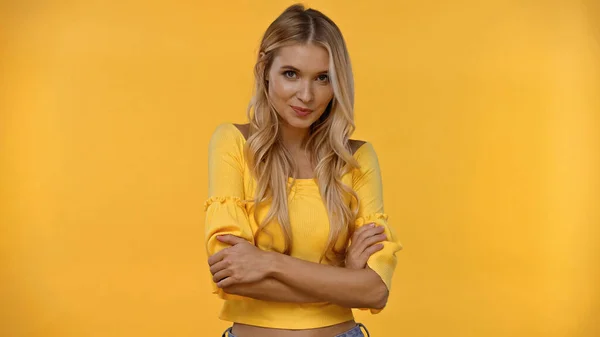 Lächelnde blonde Frau verschränkt die Arme isoliert auf gelb — Stockfoto