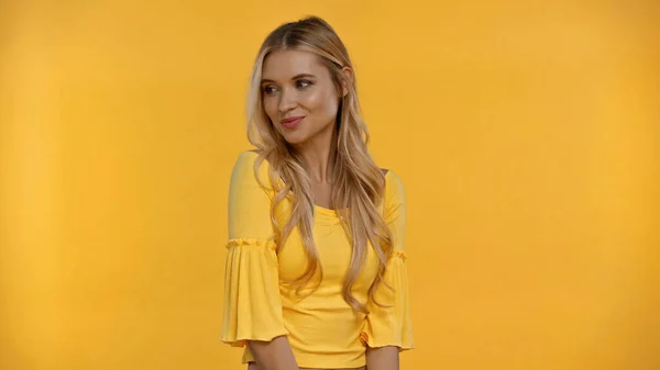 Позитивная блондинка в блузке смотрит в сторону изолированной на желтый — стоковое фото