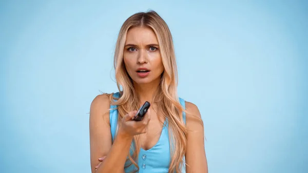 Inquiète femme blonde tenant télécommande isolé sur bleu — Photo de stock