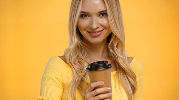 Positive blonde Frau hält Coffee to go in der Hand und blickt isoliert in die Kamera auf gelb — Stockfoto