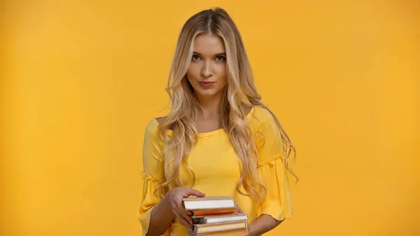 Femme blonde regardant la caméra tout en tenant des livres isolés sur jaune — Photo de stock