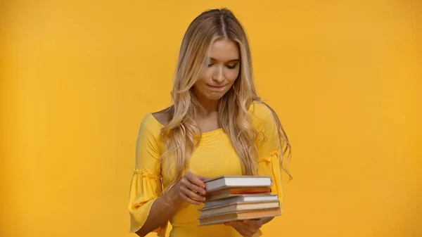 Mujer rubia pensativa sosteniendo libros aislados en amarillo - foto de stock