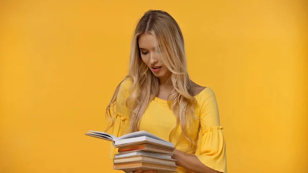 Jovem loira de blusa olhando para livros isolados em amarelo — Fotografia de Stock