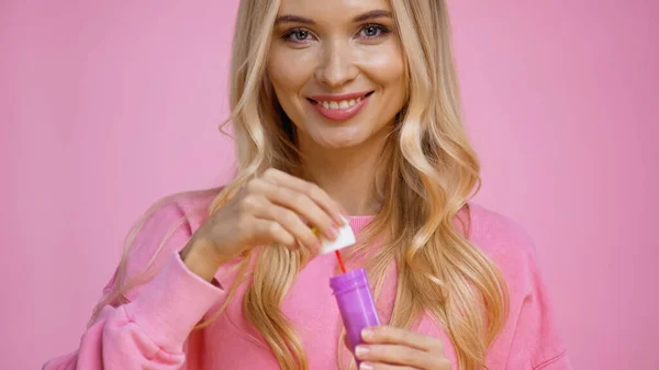 Cheerful blonde woman holding wand and soap bubbles isolated on pink — Stock Photo