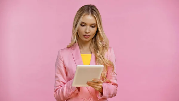 Mujer rubia con chaqueta usando tableta digital aislada en rosa - foto de stock