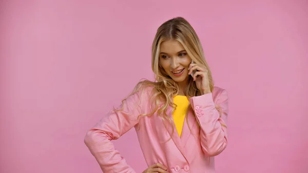 Усміхнена блондинка в куртці говорить на смартфоні ізольовано на рожевому — стокове фото