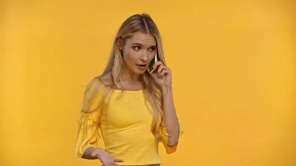 Blonde woman talking on cellphone and gesturing isolated on yellow — Stock Photo