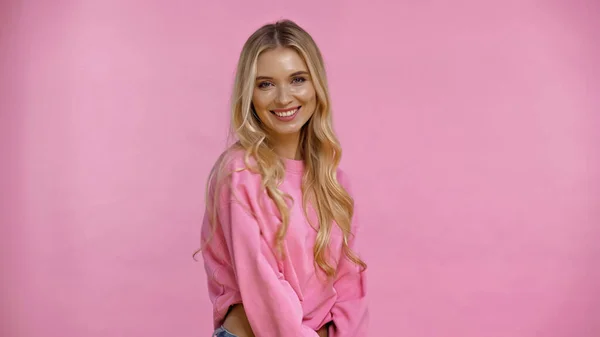Happy blonde woman in sweatshirt looking at camera isolated on pink — Stock Photo