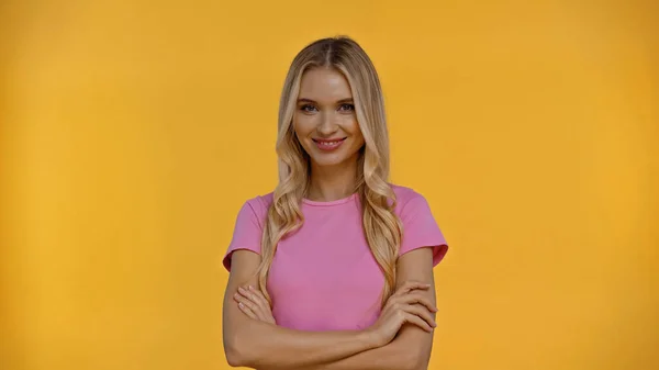 Lächelnde blonde Frau verschränkt die Arme und blickt vereinzelt in die Kamera auf gelb — Stockfoto
