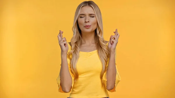 Mujer rubia en blusa cruzando dedos aislados en amarillo - foto de stock