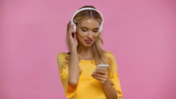 Positive woman using cellphone and headphones isolated on pink — Stock Photo