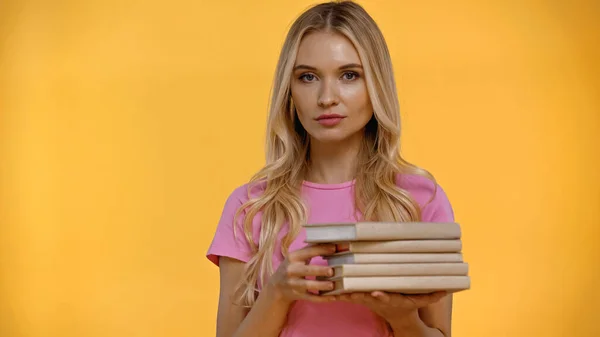 Mujer rubia sosteniendo libros borrosos aislados en amarillo - foto de stock