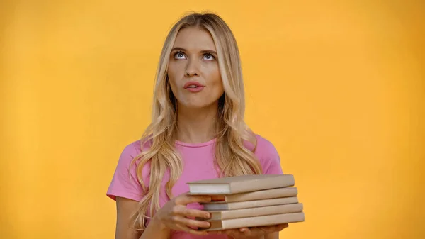 Femme blonde sceptique tenant des livres isolés sur jaune — Photo de stock